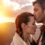 Ein junges Pärchen steht in einer Landschaft sich gegenüber. Bei geschlossenen Augen, küsst der Mann die Stirn seiner Frau. Sie machen einen glücklichen Eindruck, weil beide über ihre Probleme gespruchen haben und sie das Selbstbewusstsein ihren Partner gegenüber verstärken konnten. Mit ihrer Mimik strahlen sie eine gute Balance ihrer Gefühlswelt aus. Im Hintergrund ist ein roter-gelber Sonnenuntergang und Umrisse der Berggipfel zu sehen. Ein junges Pärchen steht in einer Landschaft sich gegenüber. Bei geschlossenen Augen, küsst der Mann die Stirn seiner Frau. Sie machen einen glücklichen Eindruck, weil beide über ihre Probleme gespruchen haben und sie das Selbstbewusstsein ihren Partner gegenüber verstärken konnten. Mit ihrer Mimik strahlen sie eine gute Balance ihrer Gefühlswelt aus. Im Hintergrund ist ein roter-gelber Sonnenuntergang und Umrisse der Berggipfel zu sehen.