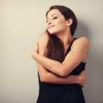 Eine junge Frau mit schwarzen langen Haaren umarmt sich selbst sehr liebevoll und lächelt verträumt dabei mit geschlossenen Augen. Sie zeigt mit ihrer Körperhaltung, dass sie ihr Selbstbewusstsein richtig stärken konnte. Sie ist bekleidet mit einem schwarzem Sommerkleid und der Hintergrund ist einfarbig braun. Das Bild insgesammt sieht sehr elegent aus. Eine junge Frau mit schwarzen langen Haaren umarmt sich selbst sehr liebevoll und lächelt verträumt dabei mit geschlossenen Augen. Sie zeigt mit ihrer Körperhaltung, dass sie ihr Selbstbewusstsein richtig stärken konnte. Sie ist bekleidet mit einem schwarzem Sommerkleid und der Hintergrund ist einfarbig braun. Das Bild insgesammt sieht sehr elegent aus.