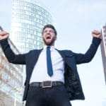 Ein Mann steht auf einer Strasse und ist bekleidet mit einem blauen Anzug und blauer Kravatte. Er hebt beide Arme nach oben und ballt seine Hände zu einer Faust. Mit seiner Gestik und Mimik drückt er aus, dass er mit dem Programm der unibee Institute, ein gutes Selbstbewusstsein erreicht hat. Er hat braune nach hinten gekämmte Haare und trägt einen Vollbart. Im Hintergrund ist die Frankfurter Skyline zu sehen. Ein Mann steht auf einer Strasse und ist bekleidet mit einem blauen Anzug und blauer Kravatte. Er hebt beide Arme nach oben und ballt seine Hände zu einer Faust. Mit seiner Gestik und Mimik drückt er aus, dass er mit dem Programm der unibee Institute, ein gutes Selbstbewusstsein erreicht hat. Er hat braune nach hinten gekämmte Haare und trägt einen Vollbart. Im Hintergrund ist die Frankfurter Skyline zu sehen.