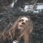 Eine junge Frau steht in einer einsamen Landschaft und die langen blonden Haare wehen im Wind. Ihr Gesichtsausdruck ist sehr Selbstbewusst und freundlich. Sie ist bekleidet mit einer dunkelblauen Windjacke und weissem Pullover. Eine junge Frau steht in einer einsamen Landschaft und die langen blonden Haare wehen im Wind. Ihr Gesichtsausdruck ist sehr Selbstbewusst und freundlich. Sie ist bekleidet mit einer dunkelblauen Windjacke und weissem Pullover.