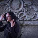 Eine junge Frau steht vor einer Klostermauer und hebt ihre Kaputze mit beiden Händen hoch. Durch den Aufenthalt in einem Kloster und den Ausdruck ihrer Gesichtsmimik hat sie deutlich mehr Selbstbewusstsein bekommen. Sie ist bekleidet mit einer schwarzen Kaputzenjacke. Eine junge Frau steht vor einer Klostermauer und hebt ihre Kaputze mit beiden Händen hoch. Durch den Aufenthalt in einem Kloster und den Ausdruck ihrer Gesichtsmimik hat sie deutlich mehr Selbstbewusstsein bekommen. Sie ist bekleidet mit einer schwarzen Kaputzenjacke.