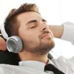 Ein junger Mann liegt auf einem Sofa und hat die Augen geschlossen. Er hat große Kopfhörer auf den Ohren und hört sich eine Hypnose CD Selbstbewusstsein stärken an. Er lächelt leicht und hat die Arme hinter seinem Kopf verschränkt. Bekleidet ist er mit einem weissen Hemd und einer schwarzen Kravatte. Der Hintergrund ist glanz weiss. Ein junger Mann liegt auf einem Sofa und hat die Augen geschlossen. Er hat große Kopfhörer auf den Ohren und hört sich eine Hypnose CD Selbstbewusstsein stärken an. Er lächelt leicht und hat die Arme hinter seinem Kopf verschränkt. Bekleidet ist er mit einem weissen Hemd und einer schwarzen Kravatte. Der Hintergrund ist glanz weiss.