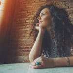 Eine Frau mittleren Alters sitzt an einem Tisch und schaut sehr Selbstbewusst in die Ferne. Sie hat sehr lange, gelockte schwarte Haare und ist bekleidet mit einem hellblauen, trägerlosem Shirt. Im Hintergrund ist eine Natursteinmauer zu sehen. Eine Frau mittleren Alters sitzt an einem Tisch und schaut sehr Selbstbewusst in die Ferne. Sie hat sehr lange, gelockte schwarte Haare und ist bekleidet mit einem hellblauen, trägerlosem Shirt. Im Hintergrund ist eine Natursteinmauer zu sehen.