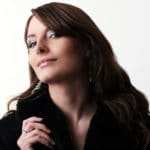 Eine Frau mit langen braunen Haaren, lächelt selbstbewusst in die Kamera. Ihre Ausstrahlung zeigt deutlich, dass Sie positiv in die Zukunft schaut und für sich selbst, die optimale Balance gefunden hat. Sie trägt einen schwarzen Mantel und der Hintergrund ist schlicht weiss. Eine Frau mit langen braunen Haaren, lächelt selbstbewusst in die Kamera. Ihre Ausstrahlung zeigt deutlich, dass Sie positiv in die Zukunft schaut und für sich selbst, die optimale Balance gefunden hat. Sie trägt einen schwarzen Mantel und der Hintergrund ist schlicht weiss.