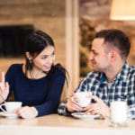 Eine Frau und ein junger Mann sitzen in einem Restaurant und trinken eine Tasse Kaffee. Beide unterhalten sich intensiv und strahlen dabei ein gutes Selbstbewusstsein aus. Sie hat lange schwarze Haare und er kurze graue Haare. Bekleidet ist die Frau mit einem dunkelblauen Pullover und der Mann trägt ein Karohemd hellblau und weiss. Eine Frau und ein junger Mann sitzen in einem Restaurant und trinken eine Tasse Kaffee. Beide unterhalten sich intensiv und strahlen dabei ein gutes Selbstbewusstsein aus. Sie hat lange schwarze Haare und er kurze graue Haare. Bekleidet ist die Frau mit einem dunkelblauen Pullover und der Mann trägt ein Karohemd hellblau und weiss.