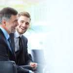 2 männliche Führungskräfte sitzen in einem Büro und lachen ausdrucksstark. Mit ihrer Ausstrahlung zeigen beide ein starkes Selbstbewusstsein, welches sie durch die Programme der unibee Institute zur Persönlichkeitsentwicklung erreicht haben. Beide sind bekleidet mit einem dunkelblauen Anzug, weissen Hemd und blauer Kravatte. Beide Männer haben kurze graue Haare und im Hintergrund ist ein Büro verschwommen zu sehen mit einem großen Bodentiefen Fenster. Weiter steht hinter den beiden Managern eine große grüne Zimmerpalme. 2 männliche Führungskräfte sitzen in einem Büro und lachen ausdrucksstark. Mit ihrer Ausstrahlung zeigen beide ein starkes Selbstbewusstsein, welches sie durch die Programme der unibee Institute zur Persönlichkeitsentwicklung erreicht haben. Beide sind bekleidet mit einem dunkelblauen Anzug, weissen Hemd und blauer Kravatte. Beide Männer haben kurze graue Haare und im Hintergrund ist ein Büro verschwommen zu sehen mit einem großen Bodentiefen Fenster. Weiter steht hinter den beiden Managern eine große grüne Zimmerpalme.